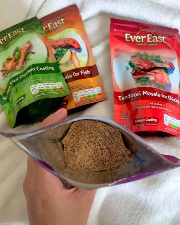 Hand holding an open pouch of spice mix beside three EverEast seasoning packets